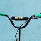 Green kids' scooter with large wheels (ages 6–12), adjustable height, rear brake, and kickstand.
