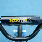 Blue kids' scooter with large wheels (ages 6–12), adjustable height, rear brake, and kickstand.